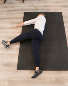 young woman lying in the start position of an eagle stretch, with hands together and one leg flexed up