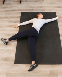 young woman lying in the end position of an eagle stretch, with arm spread apart and one leg flexed up