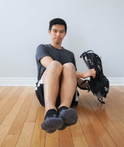 man seated on the floor holding a heavy backpack to his side ready to lift