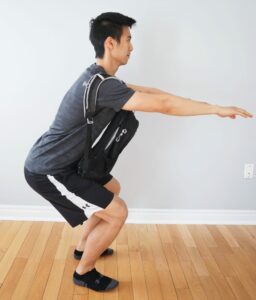 man performing a squat while wearing a heavy backpack across his chest