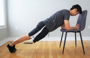 man performing a plank exercise with upper body elevated on a chair