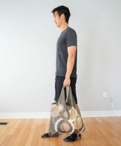 man performing a farmer's walk exercise lifting a heavy bag with one arm