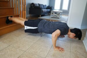 man performing a push up exercise with feet on first step of stair