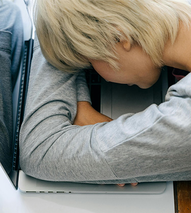 Young woman with fatigue lays her head on her laptop