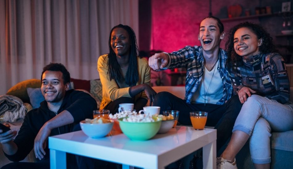 Group of diverse friends and family sit on a couch with popcorn watching a movie